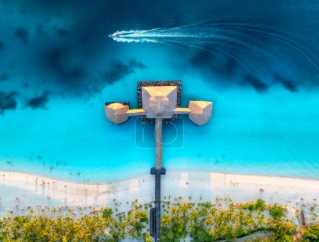 Luftaufnahme von Bungalow, Boot im Indischen Ozean bei Sonnenuntergang im Sommer. Restaurant am Meer. Drone Blick auf hölzerne Hotel, azurblaues Wasser, weißer Sandstrand, Palmen. Luxusresort in Kendwa, Sansibar