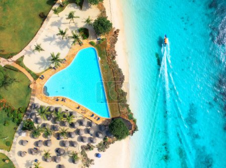 Téléchargez les photos : Vue aérienne de la piscine, plage de sable blanc avec palmiers, parasols, baigneurs, bateau, océan bleu, au coucher du soleil. Vacances d'été Nungwi, Zanzibar île. Paysage tropical. Mer claire et azur. Vue du dessus - en image libre de droit