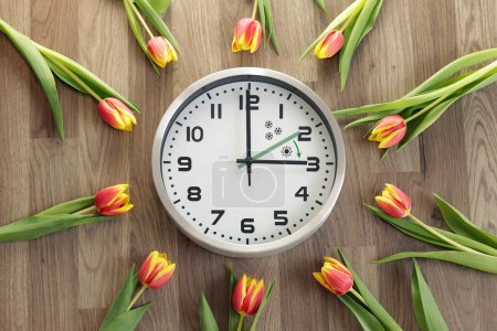 Téléchargez les photos : Une horloge montre trois heures. Les tulipes traînent. Un symbole du changement de temps. Heure d'été. Avancez les mains. La flèche verte indique la direction du mouvement des mains. - en image libre de droit