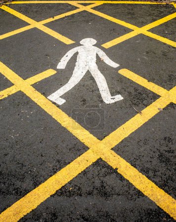 Close up of a white painted walking man in a yellow box juntion on black asphalt.