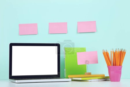Photo for Laptop computer with notepads, pencils and blank sheets of paper on blue background - Royalty Free Image