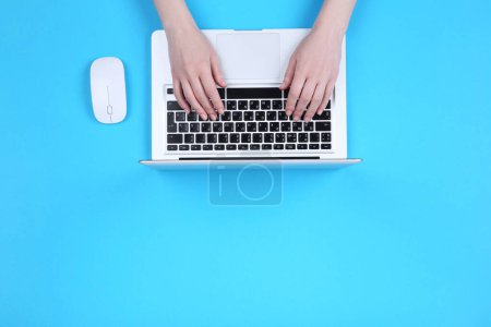 Foto de Manos femeninas escribiendo en el teclado del ordenador portátil con el ratón sobre fondo azul - Imagen libre de derechos