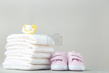 Photo for Baby diapers with pacifier and pair of shoes on grey background - Royalty Free Image