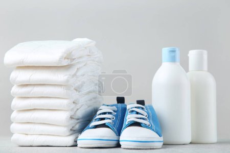 Téléchargez les photos : Couches pour bébés avec paire de chaussures et articles de toilette sur fond gris - en image libre de droit