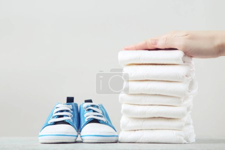Photo for Female hand on baby diapers and pair of shoes on grey background - Royalty Free Image