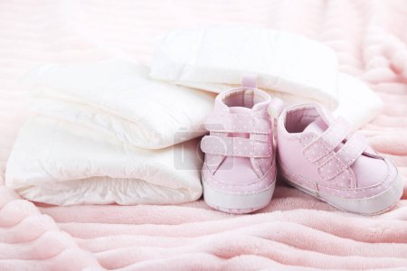 Photo for Baby diapers with pair of shoes on pink background - Royalty Free Image