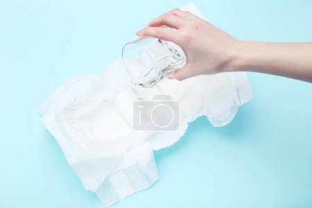 Photo for Female hand pouring water on baby diaper on blue background - Royalty Free Image