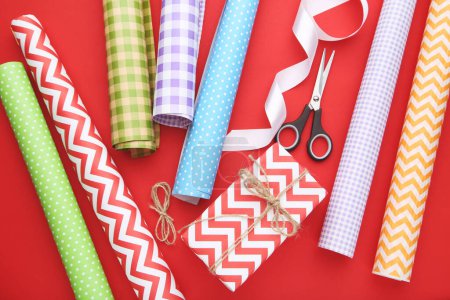 Photo for Rolls of craft papers with gift box and scissors on red background - Royalty Free Image