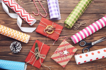 Téléchargez les photos : Rouleaux de papier artisanal avec boîtes cadeaux, ciseaux et bonbons sur fond de bois brun - en image libre de droit