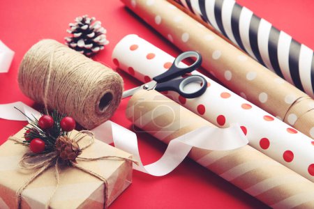 Téléchargez les photos : Rouleaux de papier artisanal avec boîte cadeau et ciseaux sur fond rouge - en image libre de droit