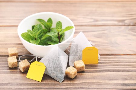 Téléchargez les photos : Sachets de thé avec des cubes de sucre et des feuilles de menthe sur une table en bois - en image libre de droit