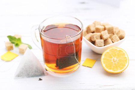 Foto de Taza de té con limón, terrones de azúcar y bolsa de té sobre mesa de madera blanca - Imagen libre de derechos