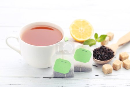 Foto de Taza de té con bolsitas de té, terrones de azúcar y limón sobre mesa de madera blanca - Imagen libre de derechos