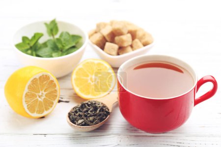 Téléchargez les photos : Tasse de thé aux citrons, feuilles de menthe et cubes de sucre sur table en bois blanc - en image libre de droit