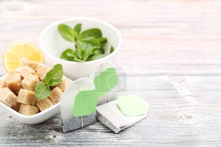 Foto de Bolsas de té con hojas de menta, terrones de azúcar y limón sobre mesa de madera - Imagen libre de derechos