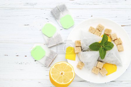 Photo for Tea bags with lemon, mint leafs and sugar cubes on white wooden table - Royalty Free Image