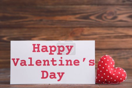 Foto de Corazón de tela y texto Feliz día de San Valentín sobre fondo de madera marrón - Imagen libre de derechos