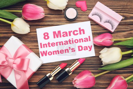 Foto de Flowers of tulips, lipsticks, eyelashes and gift box and card with text 8 March International Women's Day on brown wooden background - Imagen libre de derechos