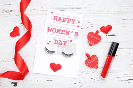 Foto de Card with text Happy Women's Day in envelope. Ribbon and hearts, clothespins and red lip gloss on white wooden background - Imagen libre de derechos