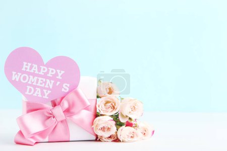 Téléchargez les photos : Bouquet de roses, cadeau et carte en forme avec texte Happy Women's Day sur fond bleu - en image libre de droit