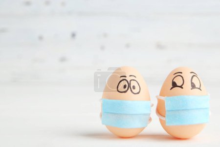 Photo for Chicken eggs in medical mask with funny faces on white wooden background - Royalty Free Image