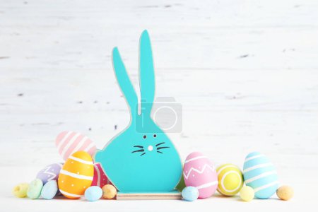Foto de Conejo de madera y coloridos huevos de Pascua sobre fondo blanco - Imagen libre de derechos