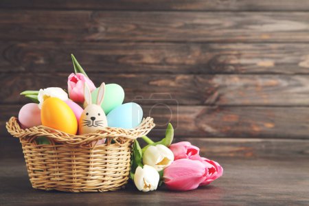 Téléchargez les photos : Colorful easter eggs in basket, egg in shape of rabbit and flowers of tulips on dark brown wooden background - en image libre de droit
