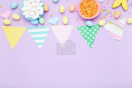Foto de Concepto de Pascua. Banderas de papel con huevos, malvaviscos y salpicaduras sobre fondo púrpura - Imagen libre de derechos