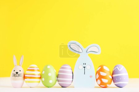 Photo for Easter eggs and wooden rabbits in row on yellow background - Royalty Free Image