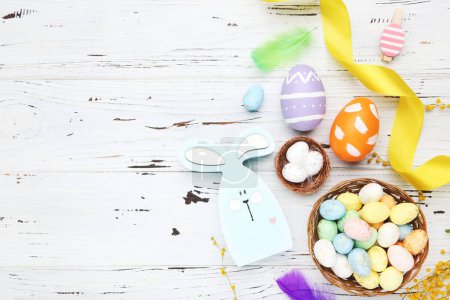 Photo for Colorful eggs in baskets, clothespins, ribbon, feathers and rabbit on white wooden background - Royalty Free Image