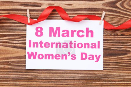 Téléchargez les photos : Carte avec texte 8 Mars Journée internationale de la femme accrochée au ruban rouge, sur fond de bois brun - en image libre de droit