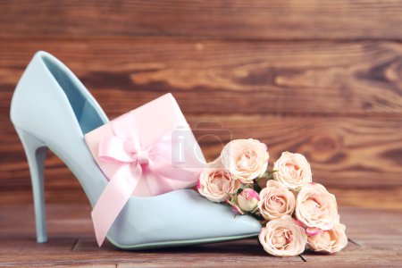 Photo for Flowers of roses, gift box and blue high-heeled shoe on brown wooden background - Royalty Free Image