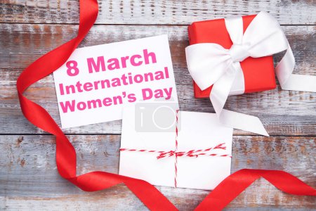 Téléchargez les photos : Carte avec texte 8 Mars Journée internationale de la femme, enveloppe avec lettre, cadeau et ruban rouge sur fond en bois - en image libre de droit