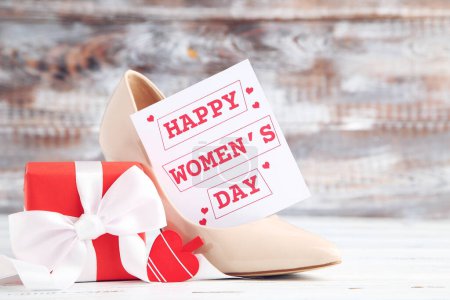 Téléchargez les photos : Carte avec texte Happy Women's Day, cadeau et chaussure à talons hauts beige sur fond en bois - en image libre de droit