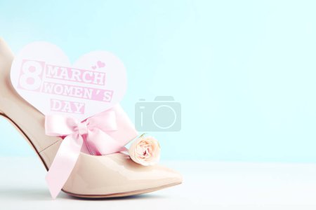 Foto de Flor de rosa, regalo y tarjeta en forma de con texto 8 Marzo Día de la Mujer, y zapato de tacón alto beige sobre fondo azul - Imagen libre de derechos