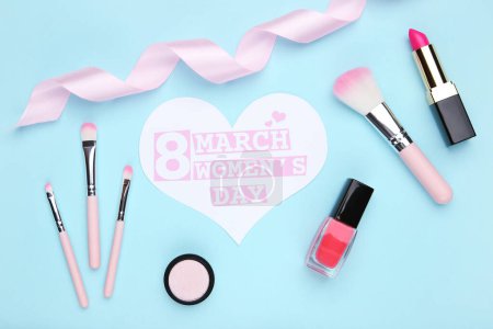 Photo for Card in shape of heart with text 8 March Women's Day, ribbon, makeup brush set, nail polish and lipstick on blue background - Royalty Free Image