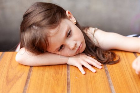 Téléchargez les photos : Portrait d'une jolie petite fille allongée sur la table en bois. - en image libre de droit