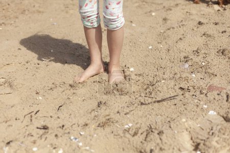 Kleines Mädchen spaziert im Sommer am Strand im Sand.