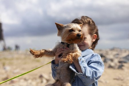 Téléchargez les photos : Petite fille avec un chien Yorkshire Terrier en promenade sur la plage - en image libre de droit