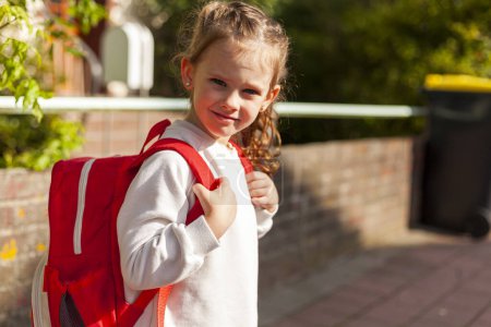 Linda colegiala con mochila roja va a la escuela en un día soleado