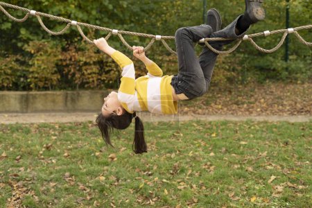 Teenage girl having fun on a rope playground in autumn park.