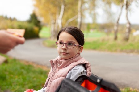 Retrato de una linda niña con gafas sentadas en la carretera