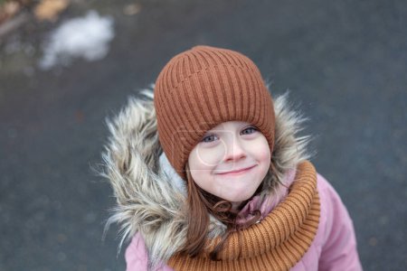 Outdoor portrait of a cute little girl wearing warm hat and scarf