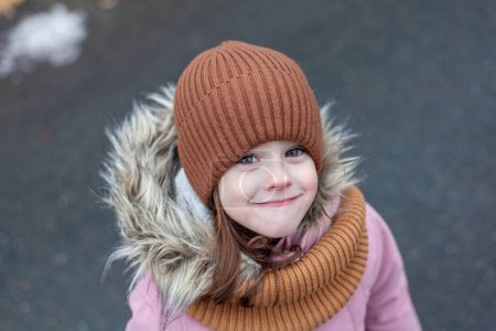 Portrait of a little girl in a warm hat and scarf outdoors