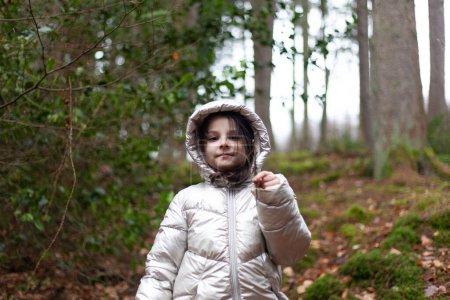 Little girl in a white jacket walks through the forest. The child is dressed in a jacket.