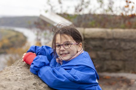 Portrait of a little girl in a blue raincoat and glasses