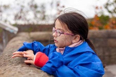 Portrait of a cute little girl in a blue jacket and glasses