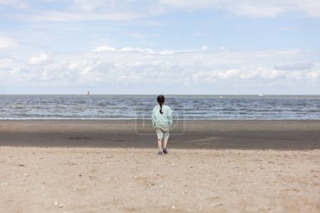 Rear view of a young woman standing on the beach and looking at the sea