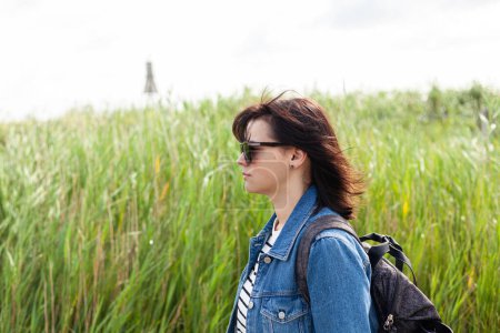 Young woman with backpack on a background of green grass and sky.