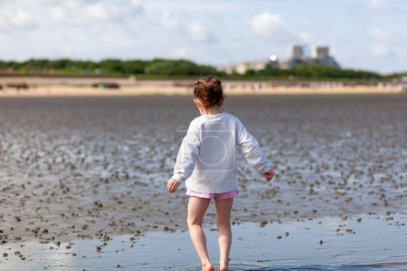 Adorable little girl having fun on a beach at low tide on a sunny day